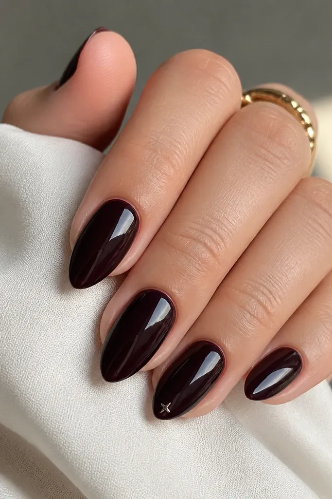 Compact short stiletto nails in glossy black cherry. One accent nail has a tiny silver micro star near the tip point, centered.