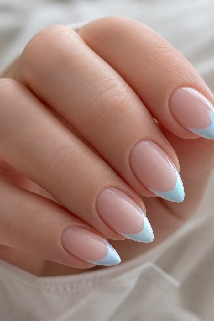 Compact short stiletto nails with a sheer nude base. The tips are painted icy blue in a narrow stiletto shape, then brushed with micro chrome powder only on the tip edge.