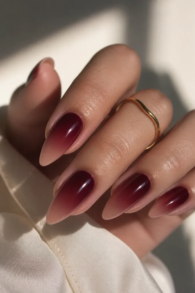 Short stiletto nails with burgundy ombre starting near the cuticle. The color fades into a nude tip, leaving the very point nude and glossy.