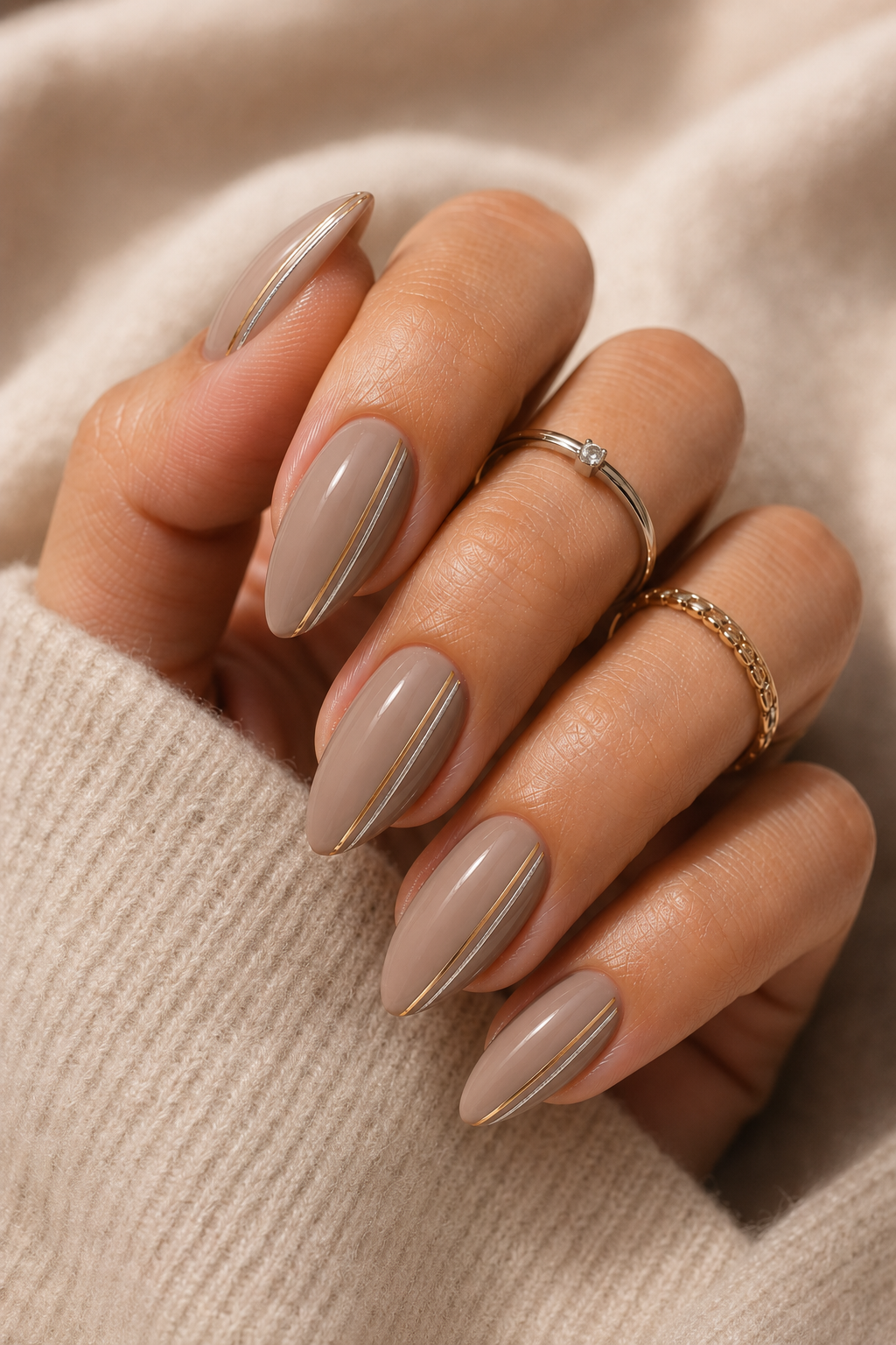 Short stiletto nails in taupe nude glossy. Two thin metallic stripes run down each side of the nail, leaving the center taupe.
