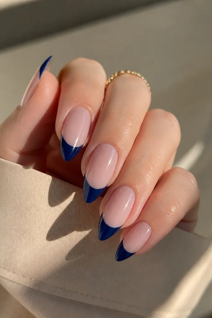 Short stiletto nails with a nude base. The French line is deep midnight blue starting near mid-nail and ending about 1 mm before the point. The tips look clean, glossy, and sharply defined.