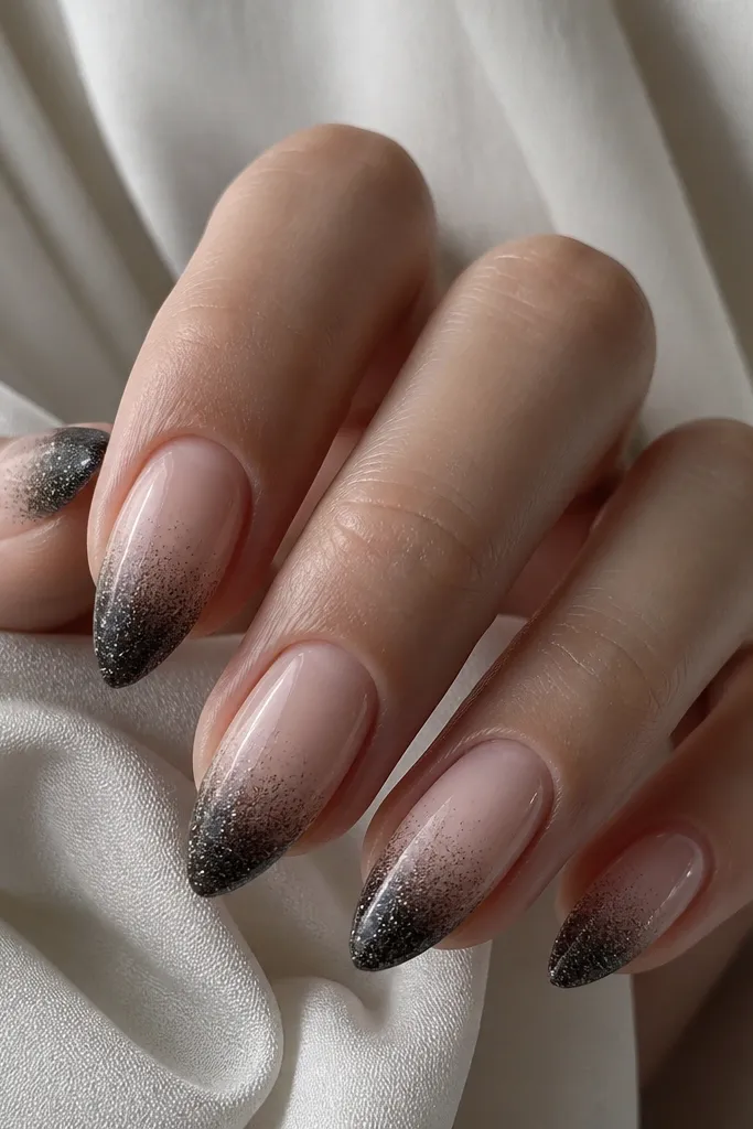 Short stiletto nails with a sheer nude base. The tips fade from solid black micro-glitter at the point into almost clear nude at mid-nail. The glitter looks fine, not chunky.