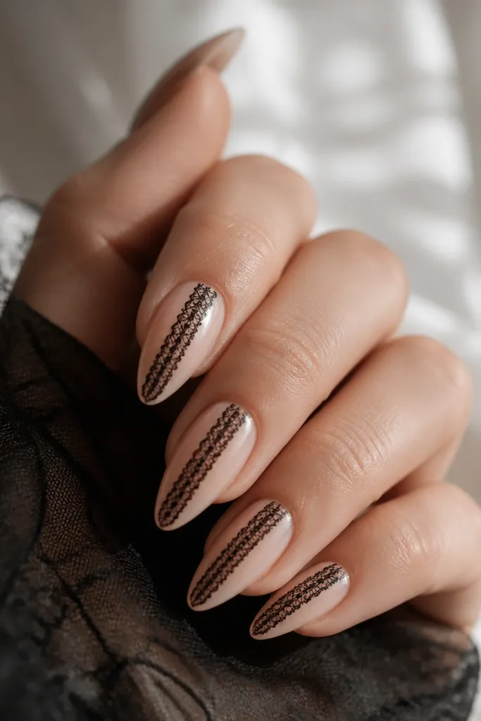 Short stiletto nails with a sheer nude base. A single vertical lace-like strip in black runs down the center, with tiny cutout patterns. The strip stops around 1-2 mm above the tip.