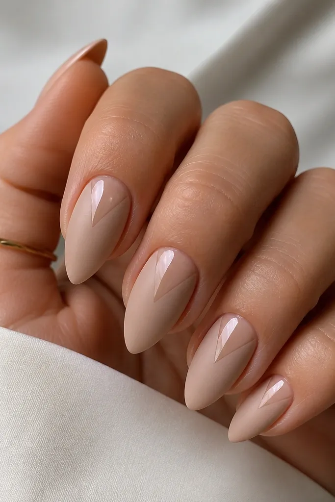 Short stiletto nails with a matte nude base. A glossy V shape sits at the cuticle area, pointing down the center toward mid-nail. The V is clean and reflective.
