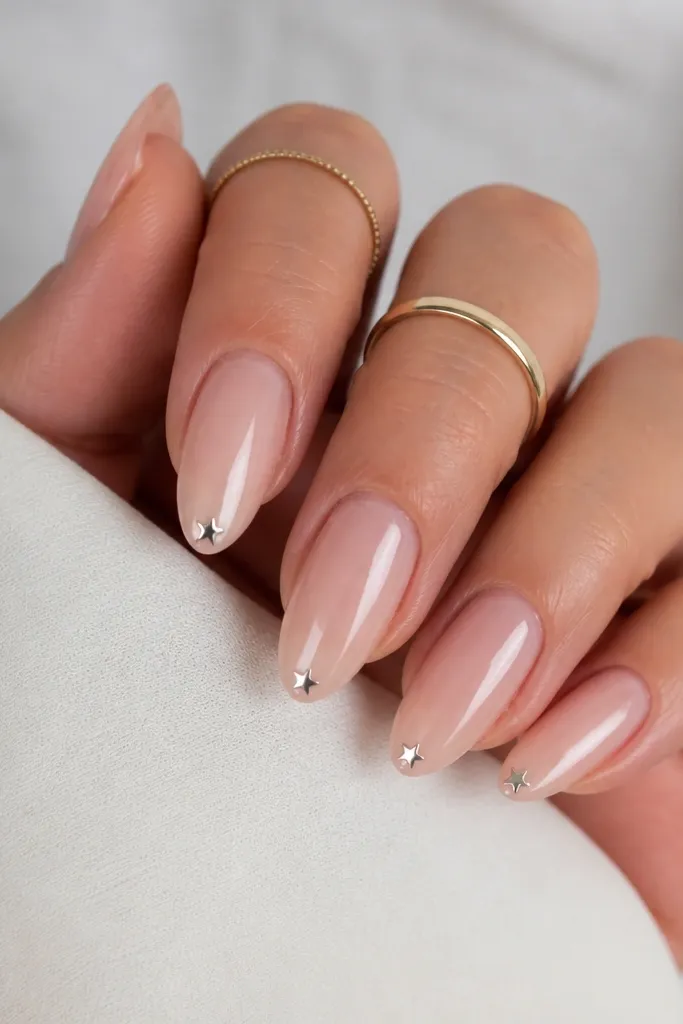 Short stiletto nails in a pearlized nude finish. On one or two nails, a tiny silver star sits about 1 mm above the tip, centered. Everything is glossy and smooth.