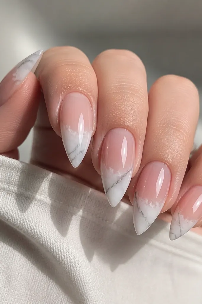 Short stiletto nails with a clear nude base. Only the tip area has white marble - thin gray veining inside a milky white tip fade. The base stays see-through.