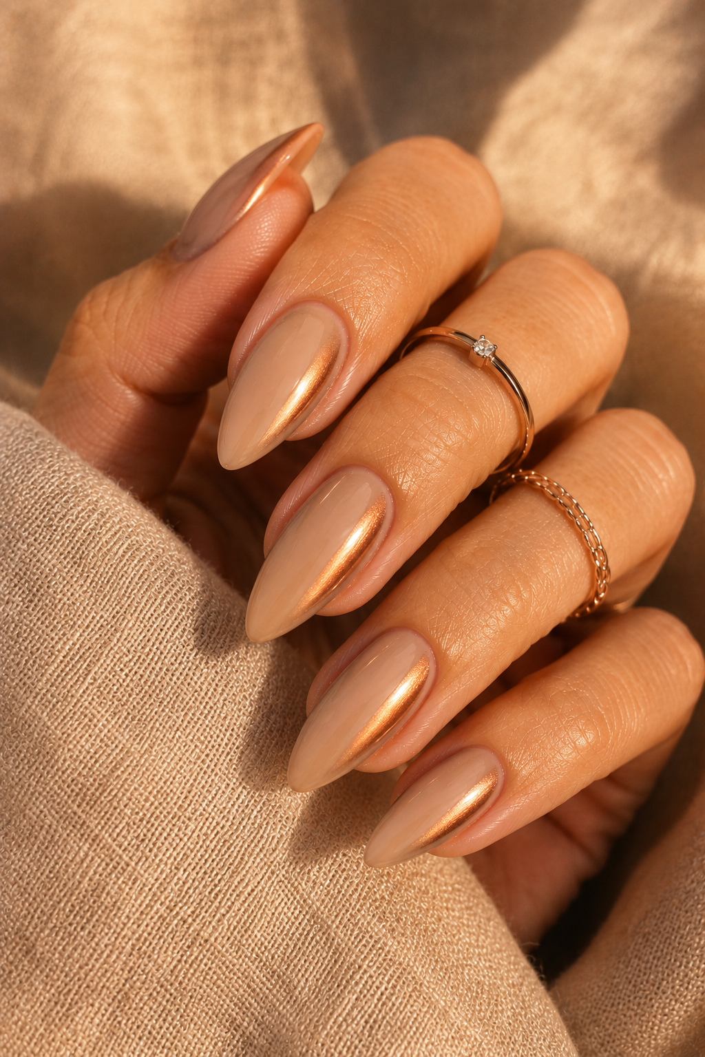 Short stiletto nails with a beige nude glossy base. Along both sidewalls, there's a soft copper shimmer glow that fades toward the center. The center stays nude and the tip is clear.