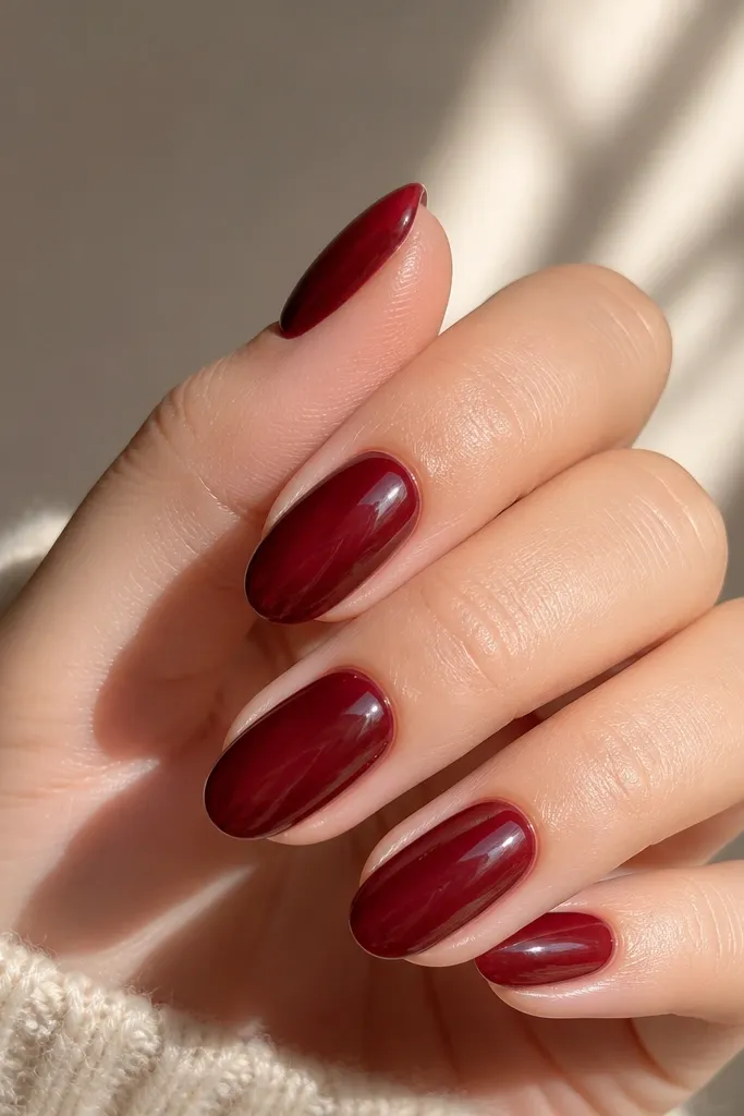 Short almond nails with a dark wine base visible near the cuticle, then a translucent deep cherry jelly layer on top, glossy finish, subtle glow at the center of each nail.