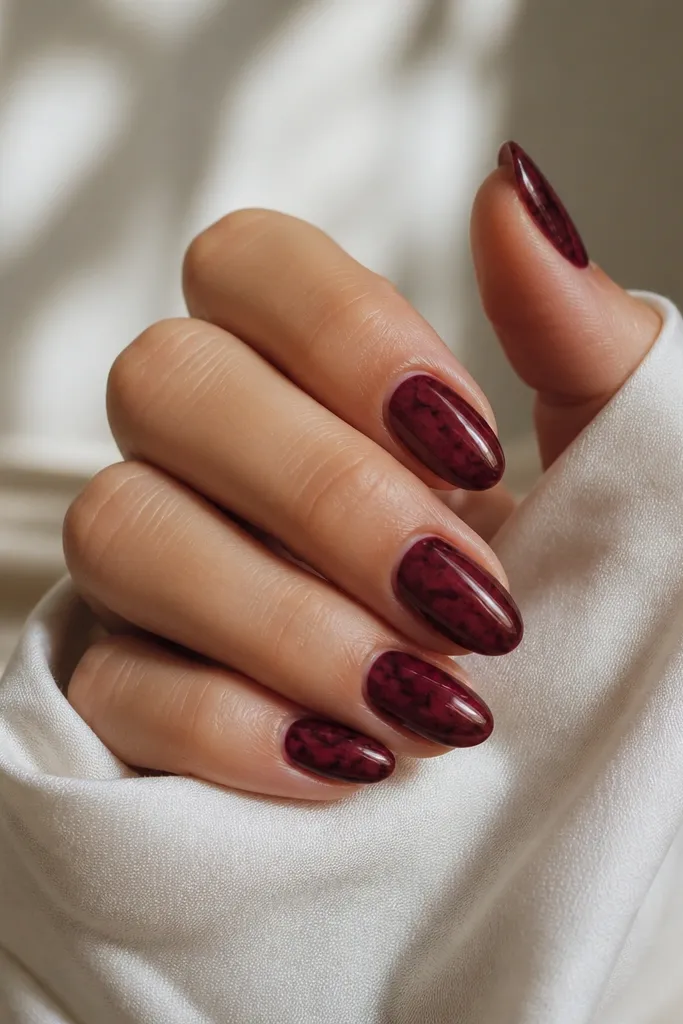 Deep cherry red nails with subtle marbled veins in darker burgundy and a hint of glossy black, glossy finish, natural stone look.
