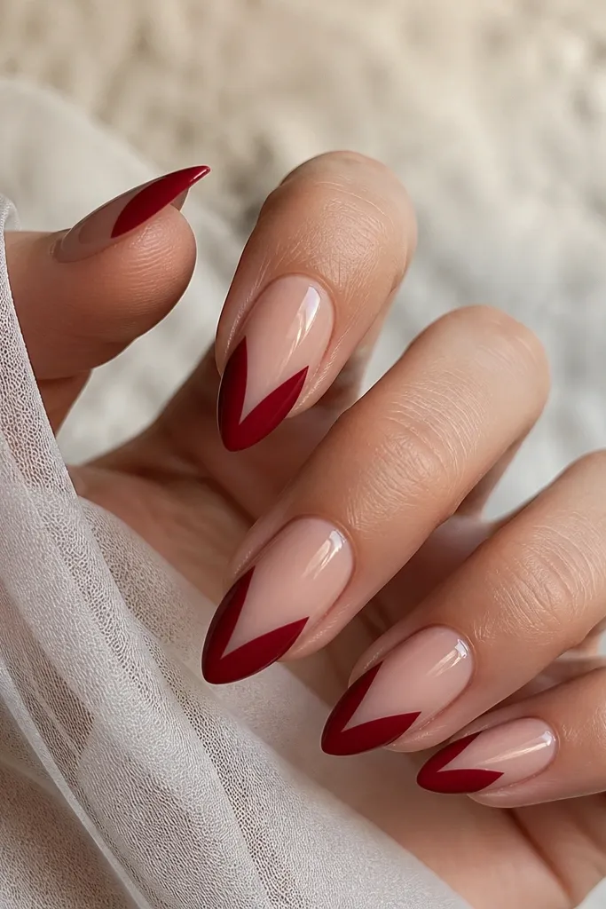 Short squoval nails: deep cherry red V shape at the tips with the rest of the nail left in a sheer nude base, glossy finish.