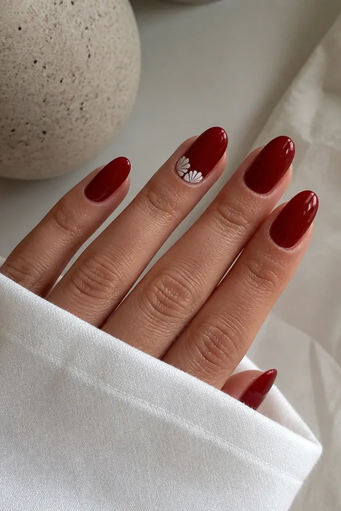 Most nails are solid deep cherry red gloss; one accent nail has small white scallop shapes near the cuticle like tiny shells, crisp lines.