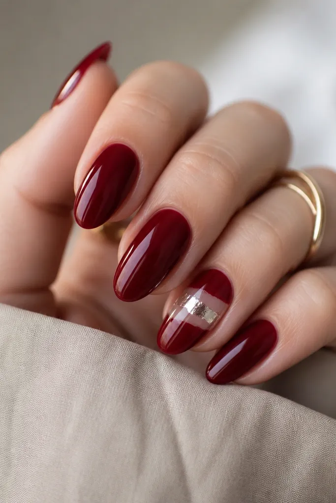 Deep cherry red nails with one accent nail featuring a glossy clear half-wrap foil effect across the middle, creating a curved reflective band.