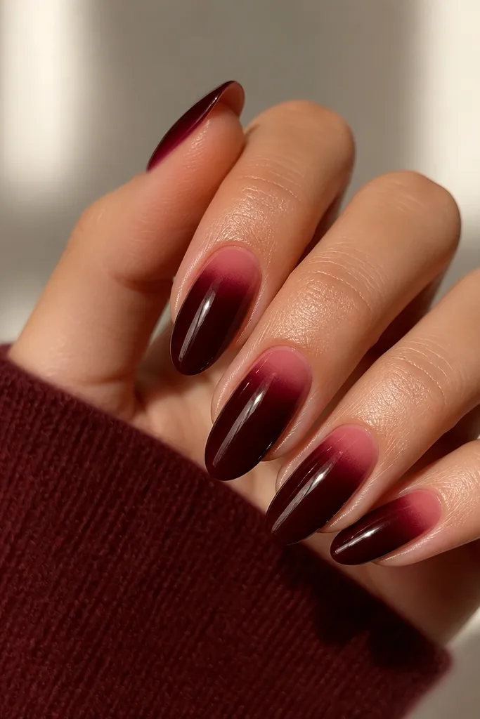 Medium almond nails in deep wine red with a subtle lighter red/rose gradient right at the cuticle, fading upward. The rest stays solid and glossy.