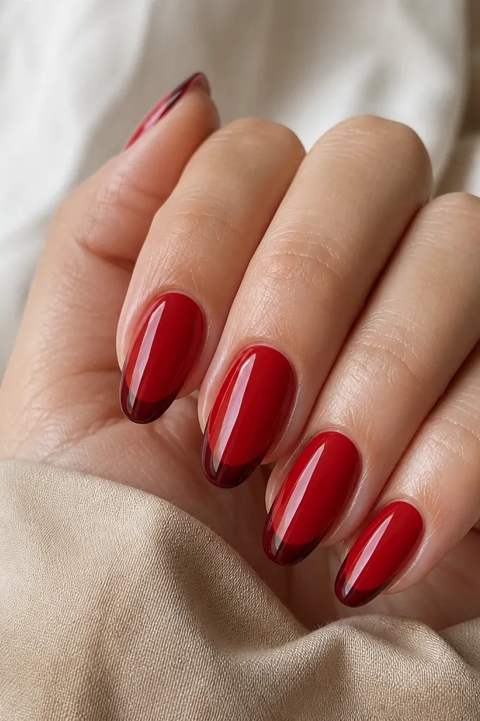 Medium almond nails with a lighter glossy red base and a darker oxblood French tip. The tip line is thin and precise, with a smooth transition.