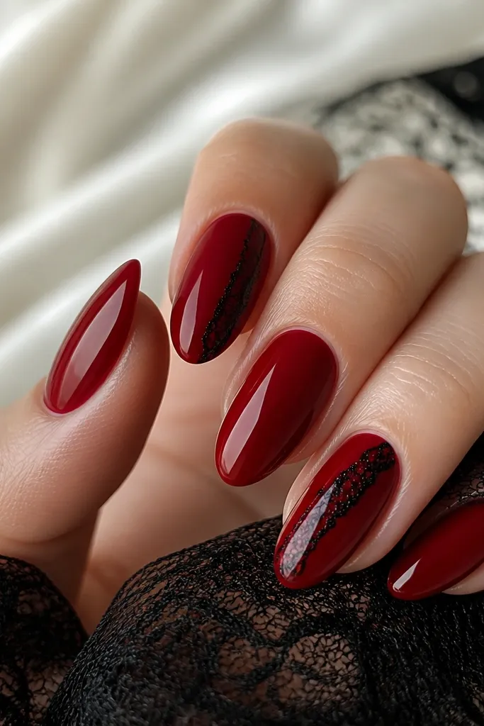 Medium almond nails in glossy deep red. On one or two nails, a thin black lace pattern runs diagonally from lower sidewall to upper tip, with the rest solid red.