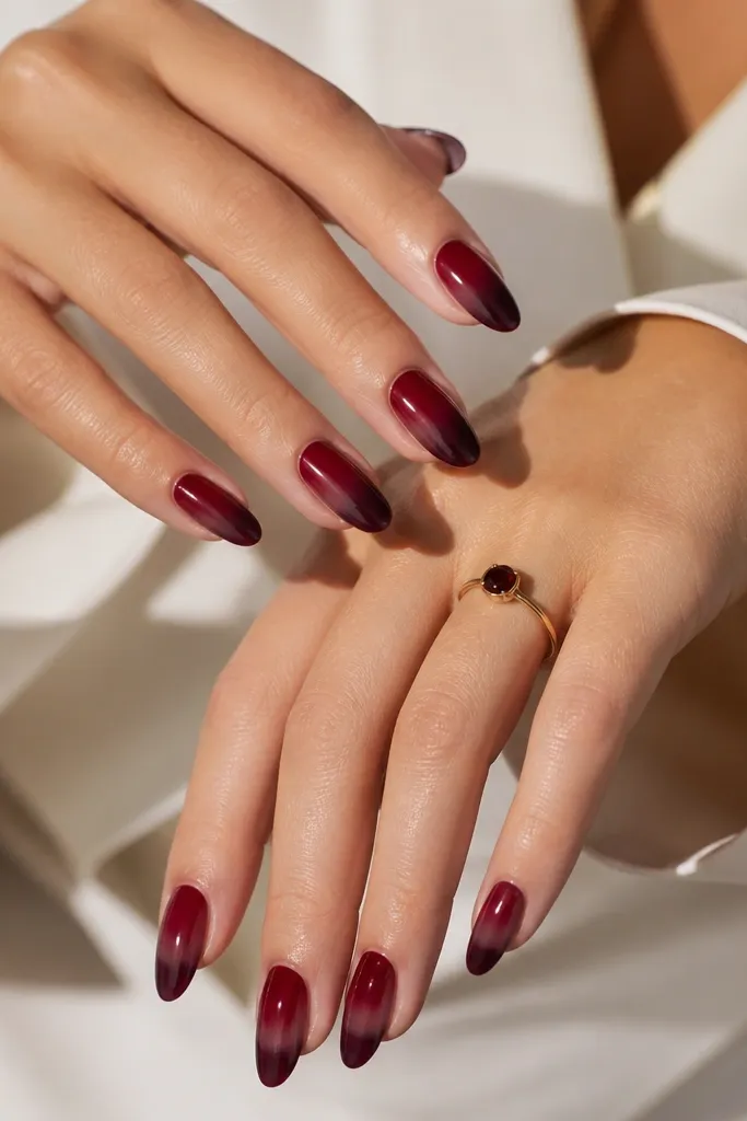 Medium almond nails with a smooth ombre that shifts from deep red at the base into softer burgundy smoke near the tips. The finish is glossy and clean.
