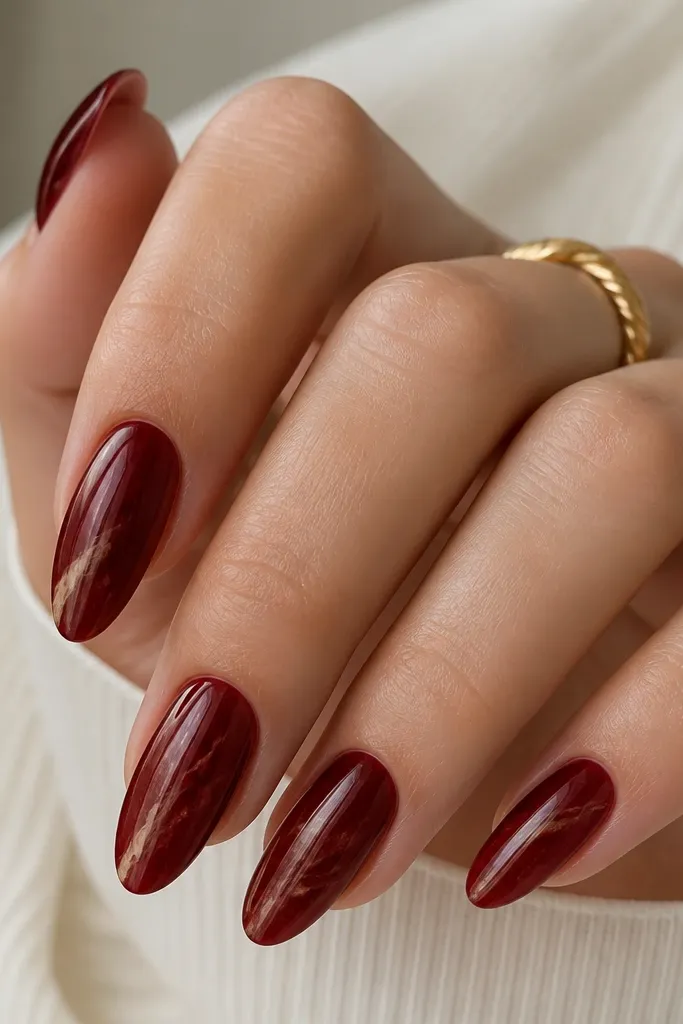 Almond nails in deep red glossy with a thin creamy latte marble vein running diagonally from near the cuticle toward the tip; the vein has soft wisps.