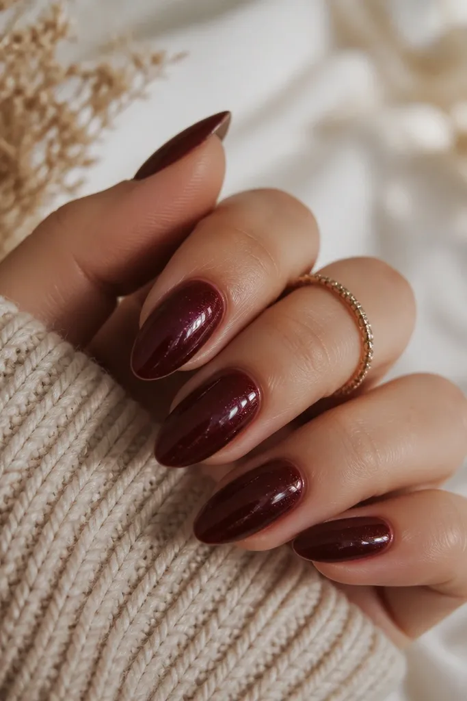 Almond nails in oxblood deep red with a fine shimmer that shows only under light; no chunky glitter, just a soft sparkle.