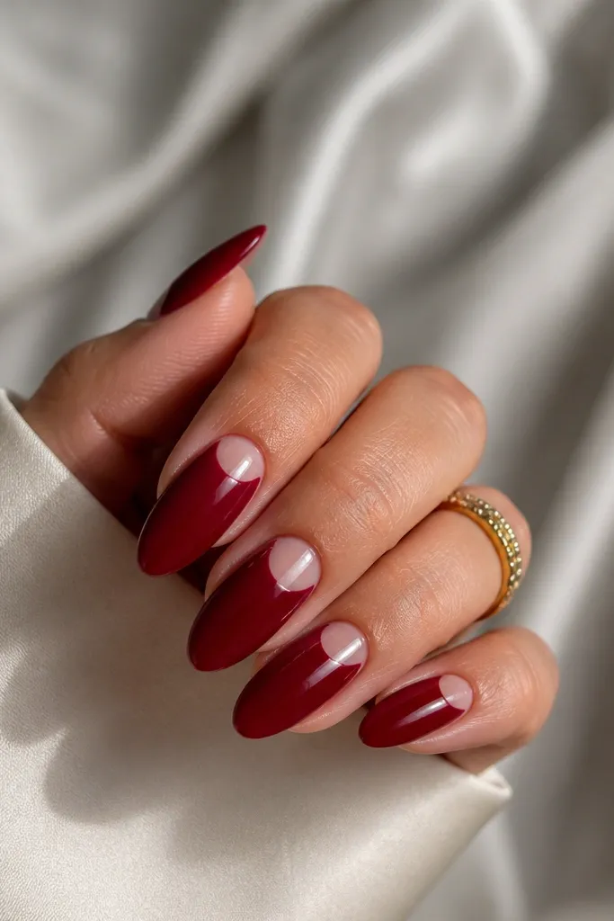 Almond nails with a glossy deep red color covering most of the nail but leaving a clear half-moon at the base near the cuticle; the half-moon is clean and rounded.