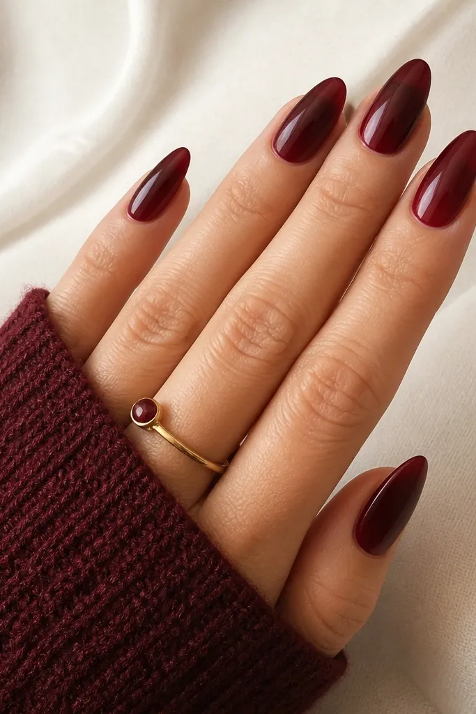 Almond nails with a deep burgundy-to-deeper-red ombré that fades smoothly from cuticle area to the tip; the transition is soft with no harsh line.