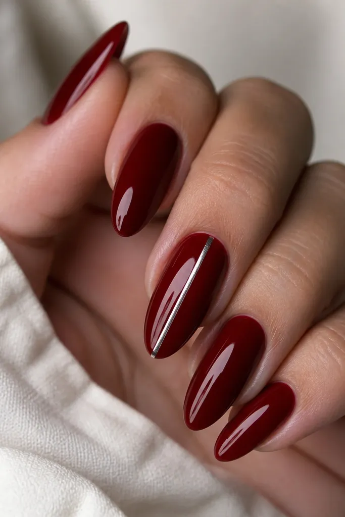 Deep red glossy almond nails with a single thin silver line running vertically down the center of one accent nail; the line is straight and mirror-like.