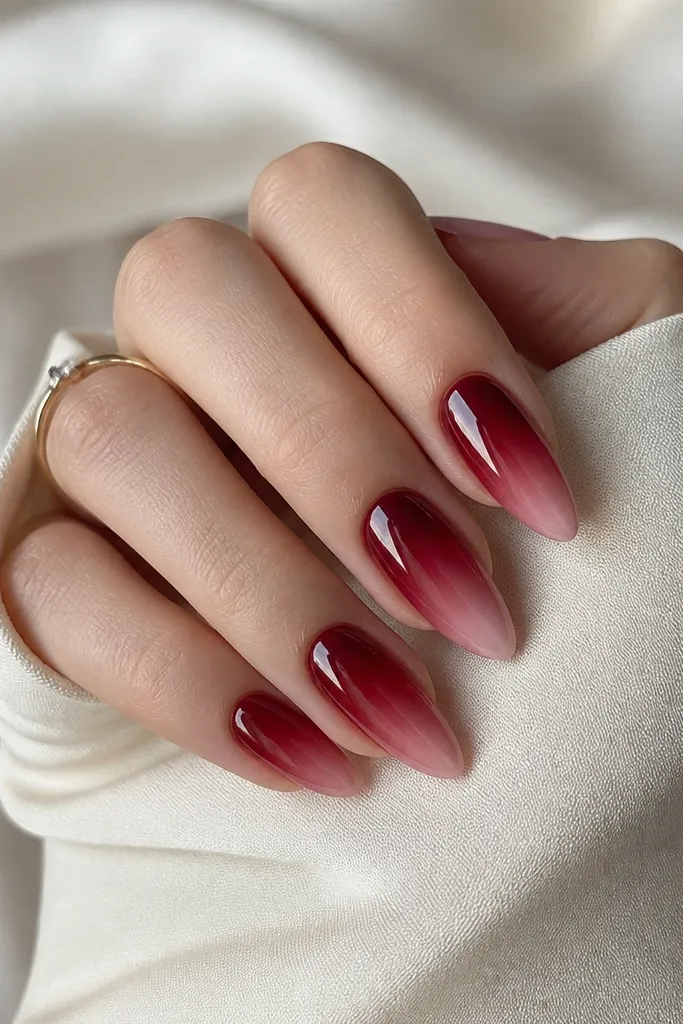 Almond nails with deep red starting near the cuticle and fading softer toward the tip. The fade looks smooth and blended, with a glossy topcoat that makes the red look dimensional.