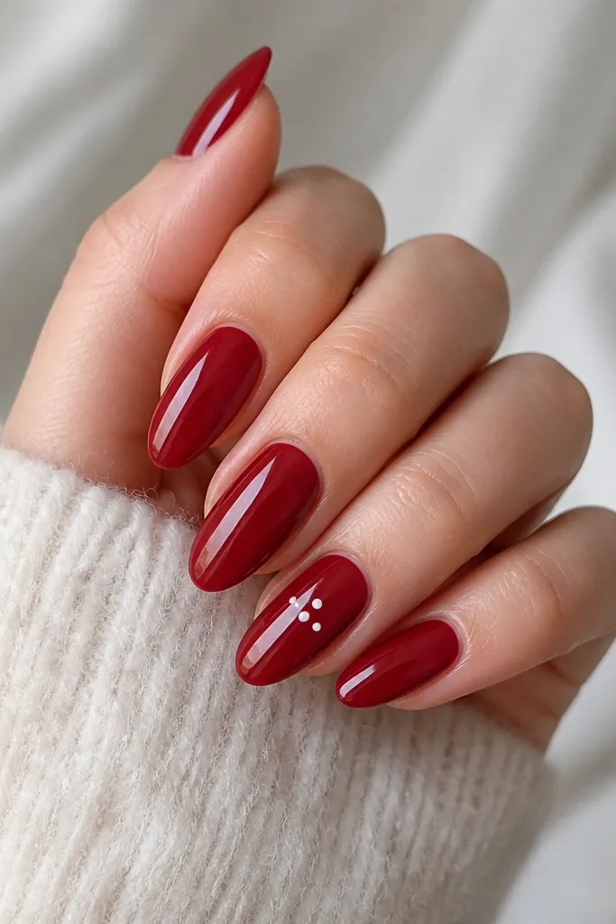 Almond nails painted glossy deep red. One accent nail has three tiny white dots aligned diagonally near the center, with crisp dot edges and no smearing.