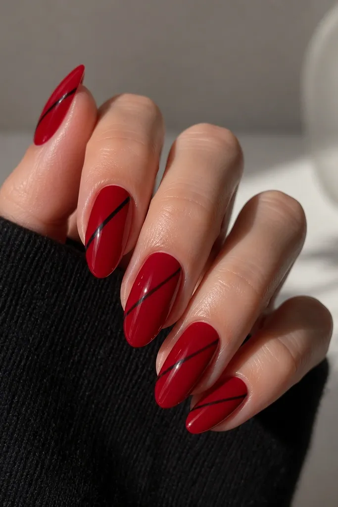 Glossy deep red almond nails. Each nail has a single thin black diagonal line from lower-left near the middle toward the upper-right near the tip. Lines are straight and crisp.