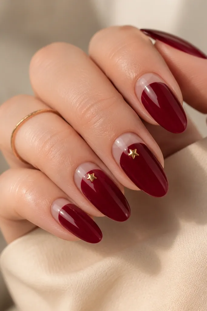 Deep oxblood nails with a half-moon cutout at the base that is bare nude. On the nude half-moon area, there are two tiny silver star studs. Everything else is glossy.