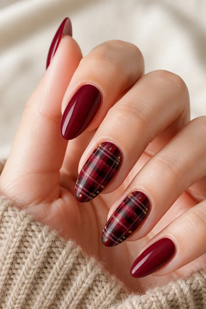 Solid deep red nails. On two accent nails, there is a red plaid pattern made with thin lines of black and pale gold, crossing diagonally and horizontally. Small gold dots sit at the intersections.