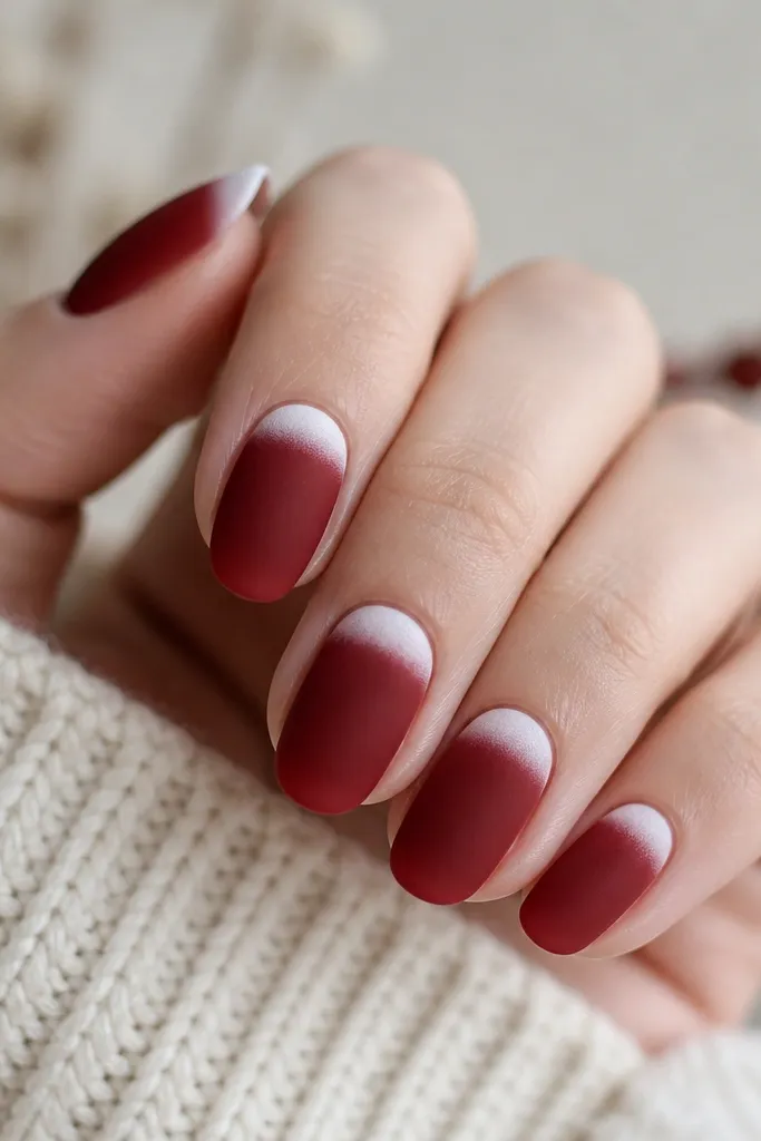 Nails are deep red with a matte velvet finish. On each nail, the top 2-3 mm has a pale icy white "snow cap" shape that fades at the edges.