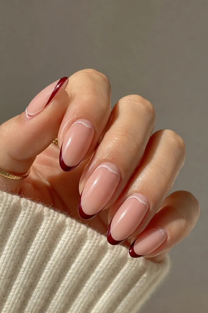 A nude base with a micro French line in burgundy at the very tip. Between the cuticle and nail bed there is a small negative space crescent that stays nude.