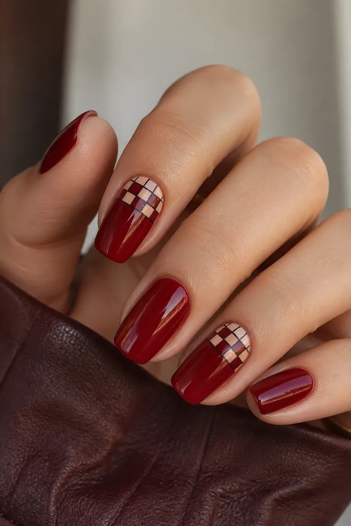 Solid glossy deep red nails. On the index and ring fingers, there is a checker accent near the tip made with small squares in deep red and pale nude, separated by thin black lines.