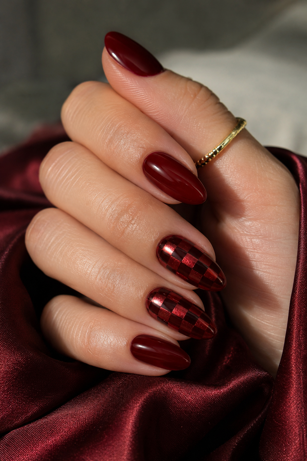 Short almond nails with deep red base; chrome forms a tiny checkered block only on the ring finger and maybe middle finger, with the rest fully deep red chrome or glossy red.
