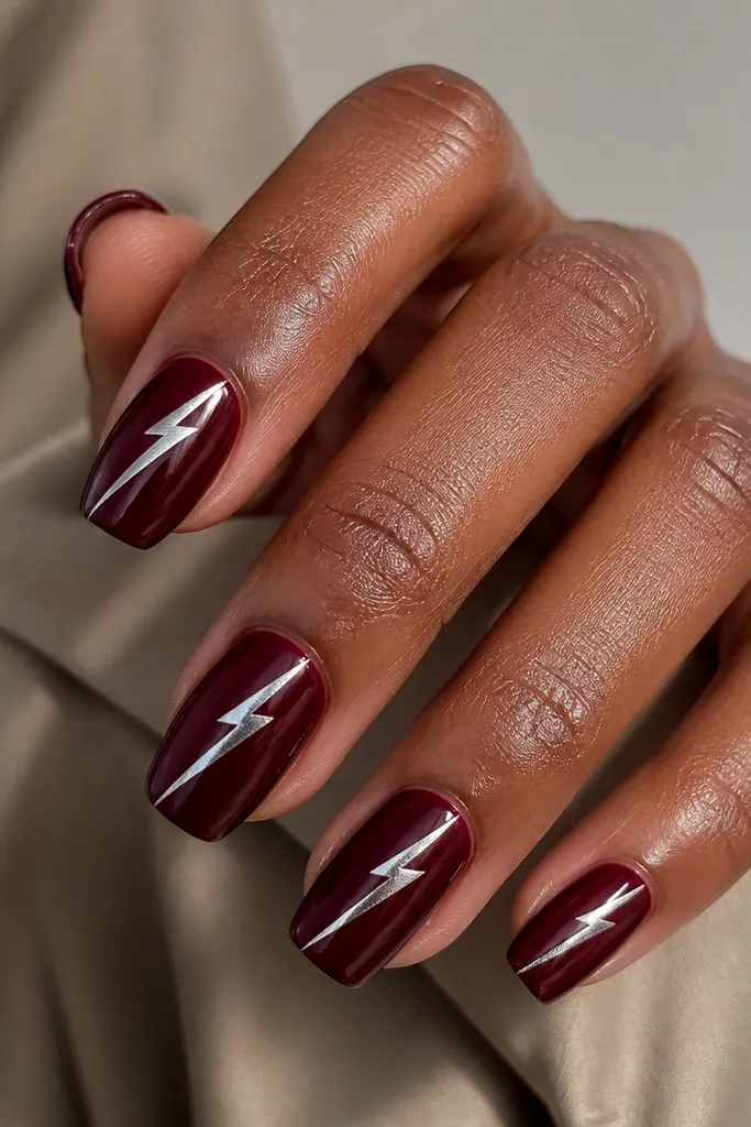 Short coffin nails with oxblood red base; a chrome lightning bolt shape runs diagonally from lower left near the cuticle to upper right toward the tip.