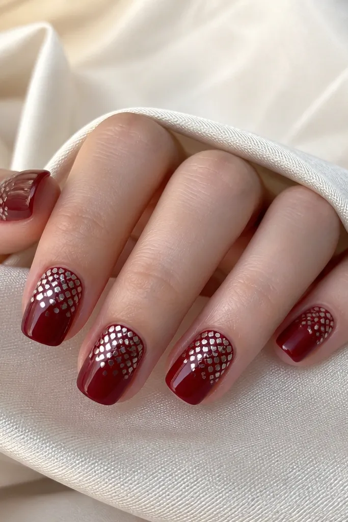 Short squoval nails with a deep red base; chrome forms a tiny checker pattern that fades from dense at the cuticle to sparse toward the tip.