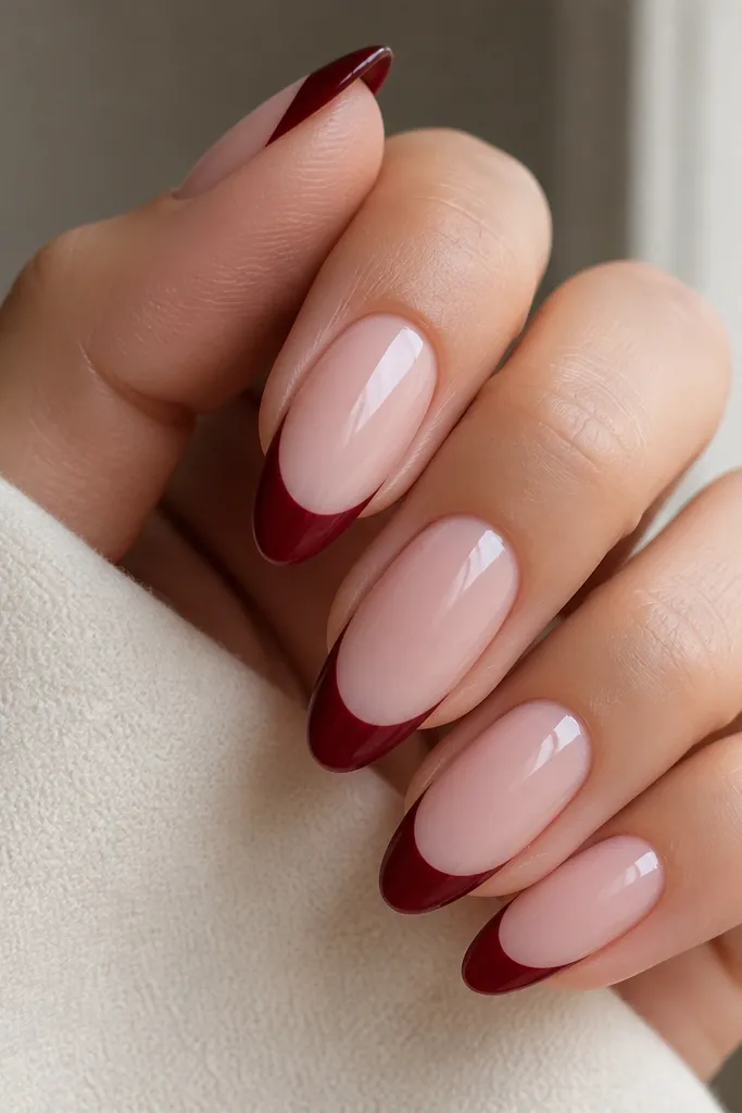 Close-up of almond nails with a glossy milky pink base; the french tips are a deep burgundy red with a perfectly smooth, curved smile line and no extra art.