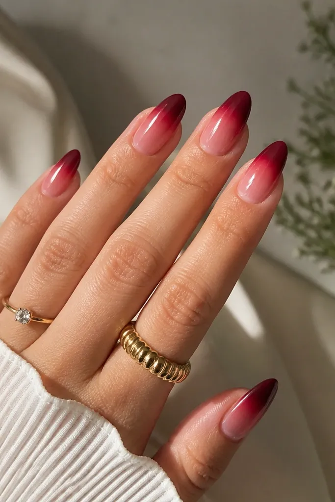 Almond nails where the tips start deep wine red and fade upward into a translucent pink gradient that blends into the base.