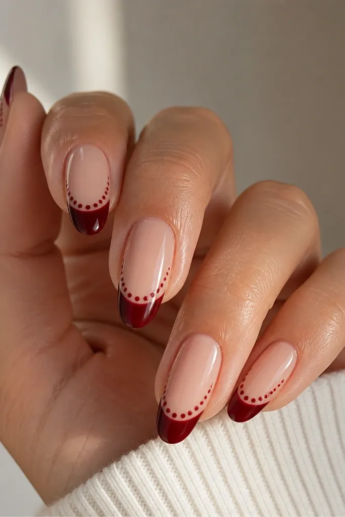 Almond nails with a glossy sheer pink base; deep red french tips and tiny micro dots in a slightly lighter burgundy following the smile line.