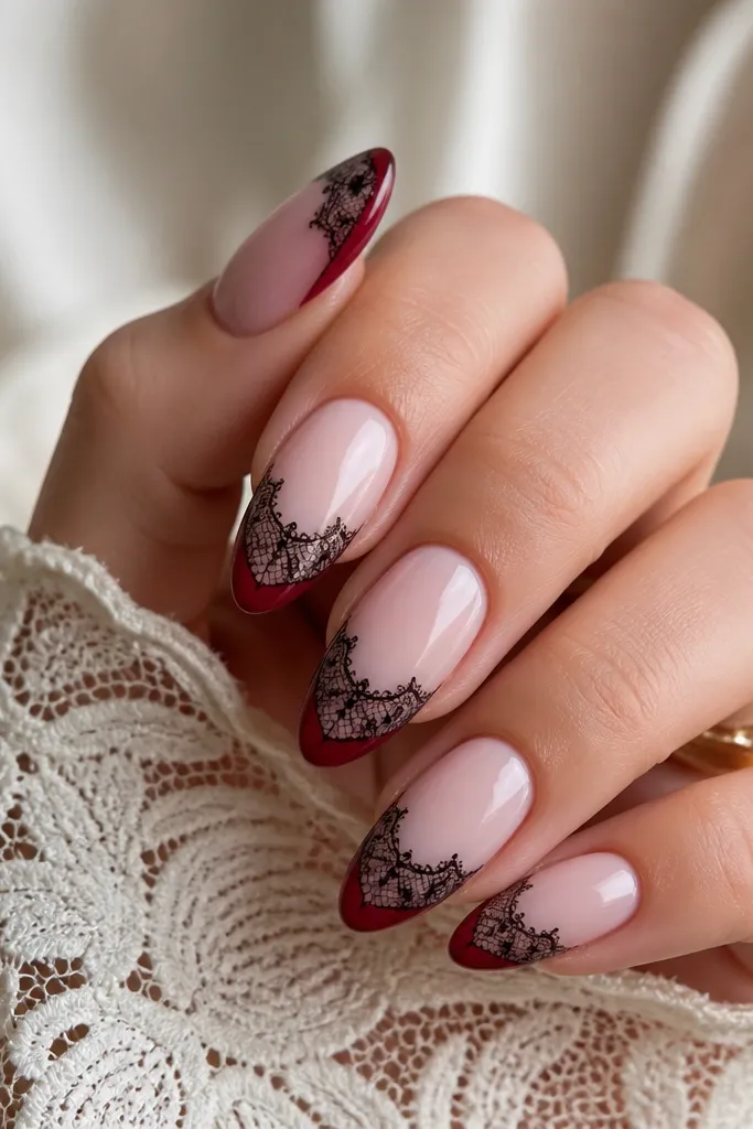 Almond nails with a milky pink base; deep red french tips covered with delicate black lace stamping near the edge.