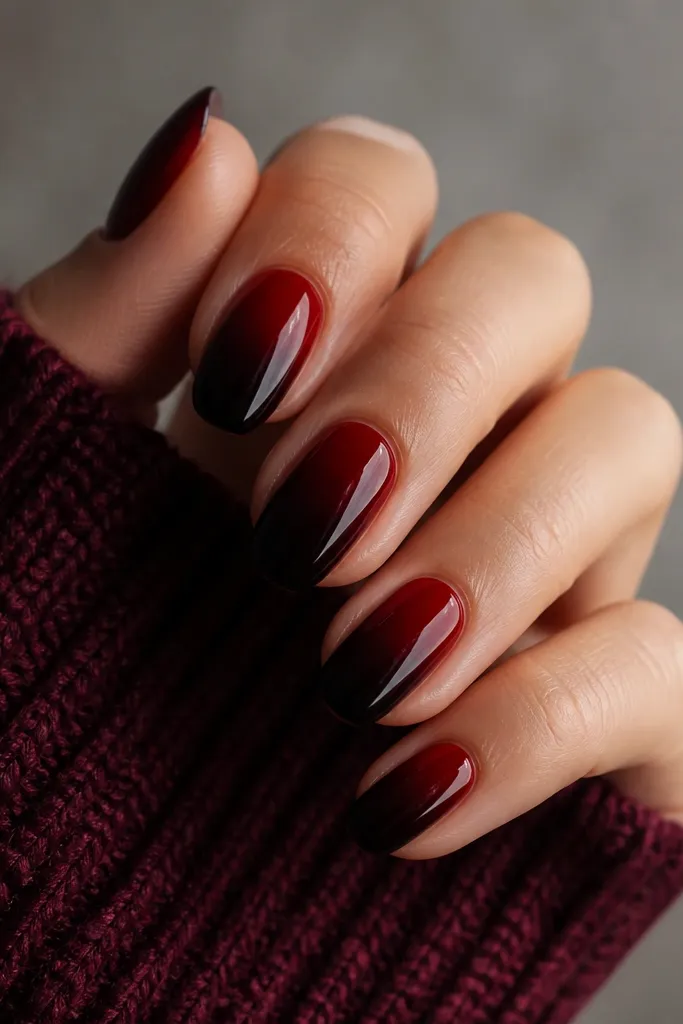 Nails painted with a smooth gradient: deep red at the base blending into darker burgundy and near-black toward the tips; glossy finish throughout.