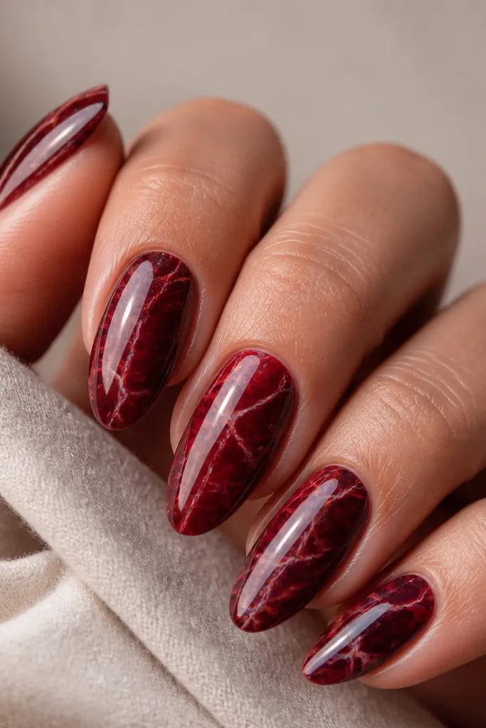 Deep red marbled nails with thin, lighter red and clear gel veins forming natural-looking cracks; glossy finish on all nails.