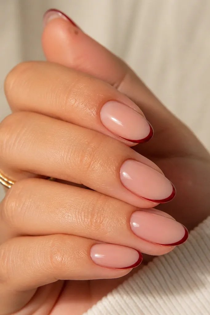 Nude base nails with very thin deep red French tips, about 1 mm wide, glossy and clean; tips are centered and even.