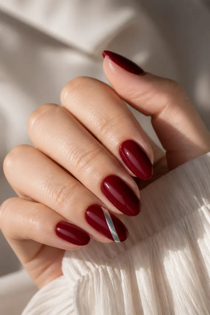 Deep red nails where one accent nail has a diagonal silver metallic stripe running from lower left near the cuticle to upper right near the tip; other nails are solid deep red.