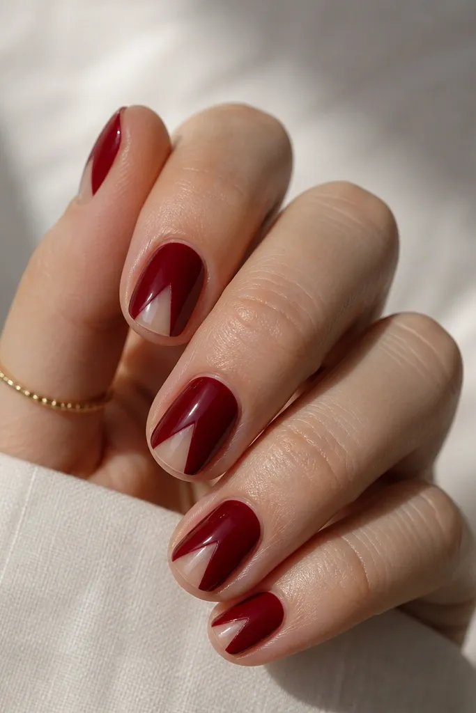 Short nails with glossy deep red base and a clear negative-space triangle at the tip area; triangle points toward the center and looks sharp and clean.