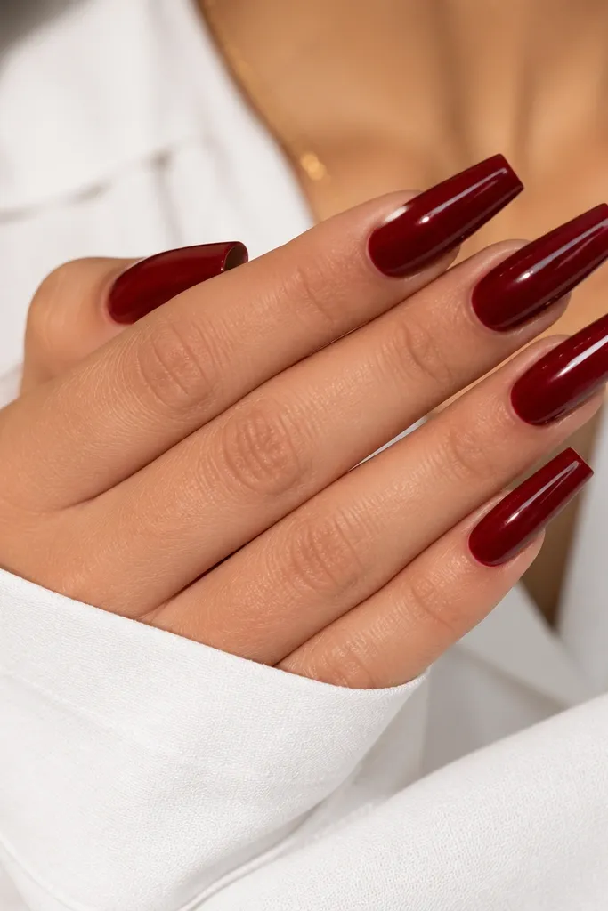 Long coffin nails in a blue-leaning deep red; the tips catch a bright reflection from a glossy finish, with a smooth, glassy surface.
