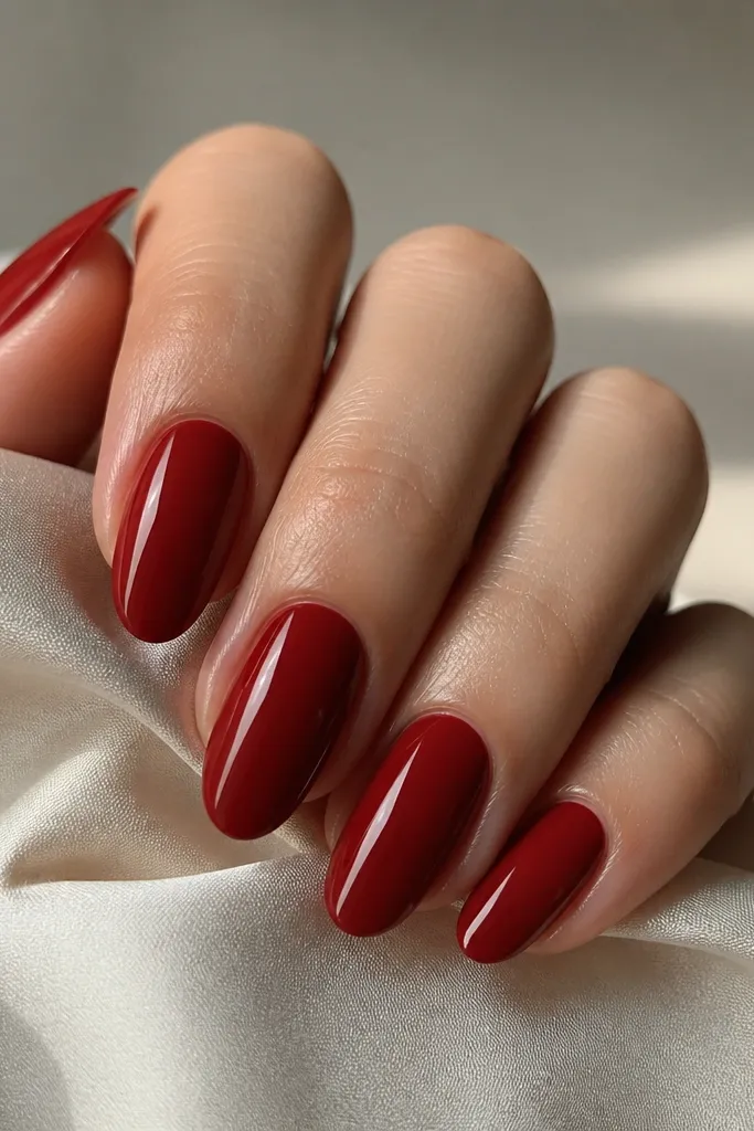 Medium almond nails in deep red with a super smooth, glassy look and ultra-clean sidewalls; the light reflection runs straight down the center.