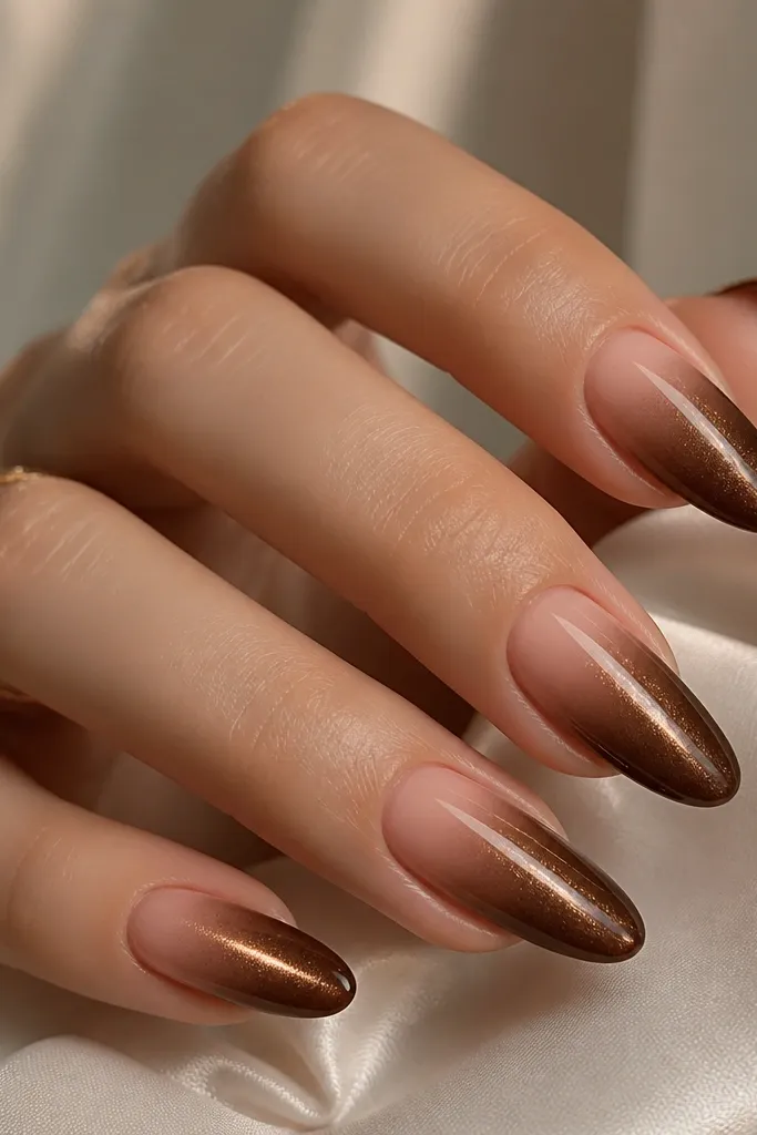 Five long almond nails. The base starts nude at the cuticle and fades into deep brown cat eye shimmer toward the tips. The cat eye stripe runs vertically within the brown area only.