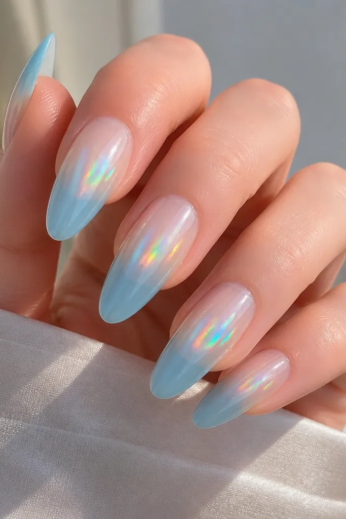 Long almond nails with sky blue ombre fading into clear; hologram chrome is placed in the center band and reflects rainbow tones.