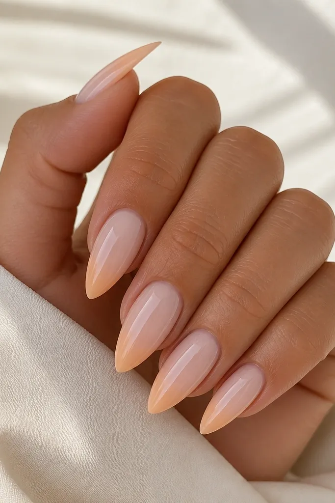 Short stiletto nails in a milky nude base. The tip fades from pale peach into the nude, forming a soft triangle that follows the stiletto taper. Everything is glossy and smooth.
